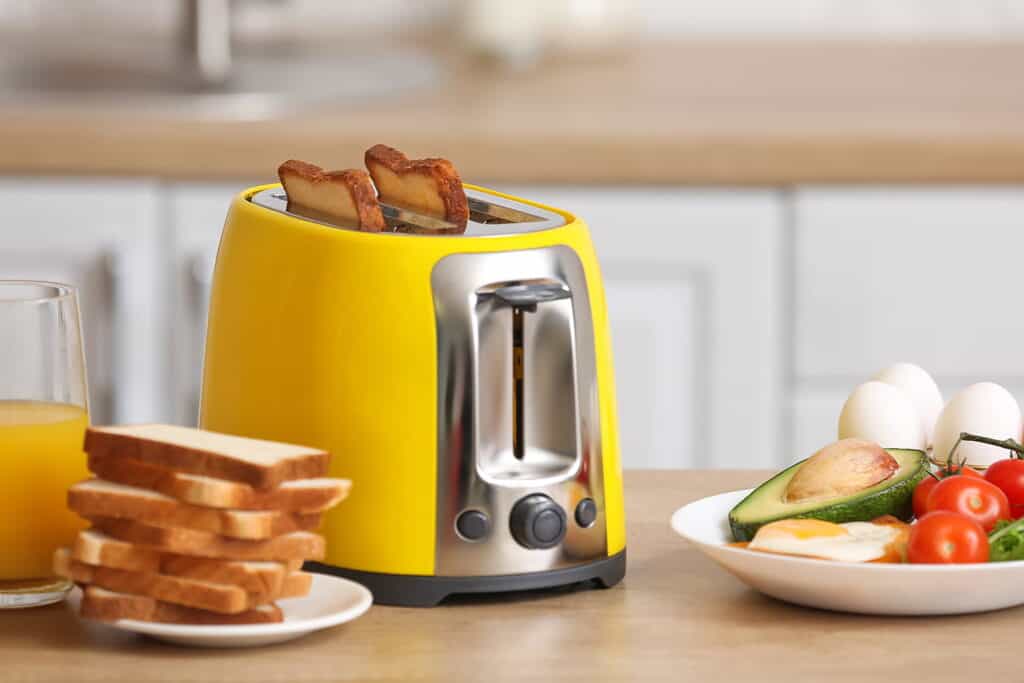 yellow toaster on a counter surrounded by juice and breakfast foods