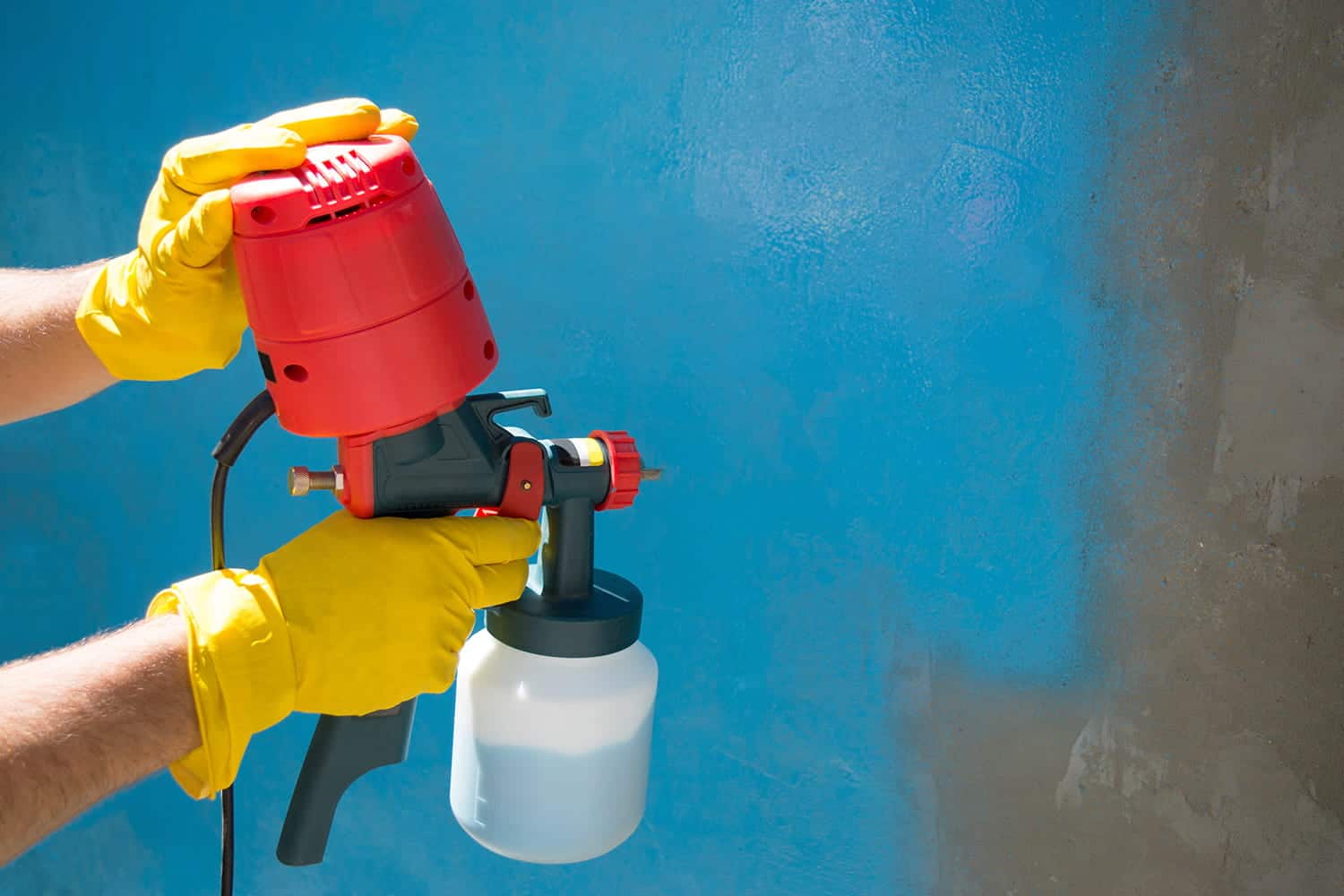 A person in yellow gloves is holding a spray gun
